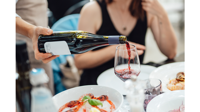 Waiter pouring wine for customers in luxury outdoor restaurant