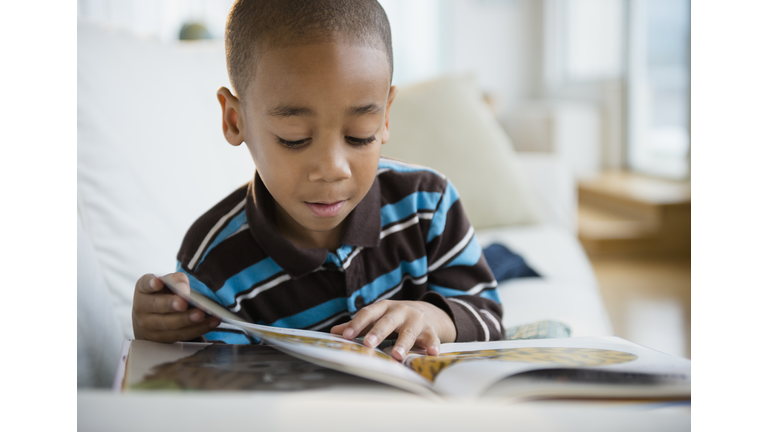 African American boy reading book on sofa
