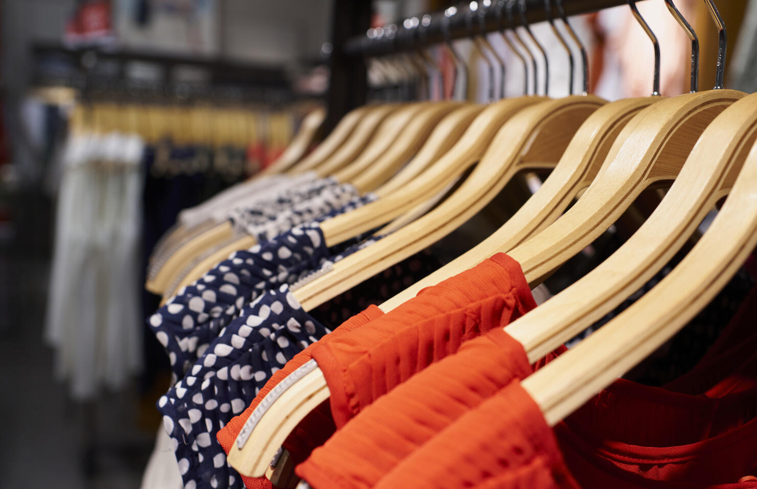Close-up view of women's dresses hanging on clothes hooks in mall store rack, latest seasonal collection.