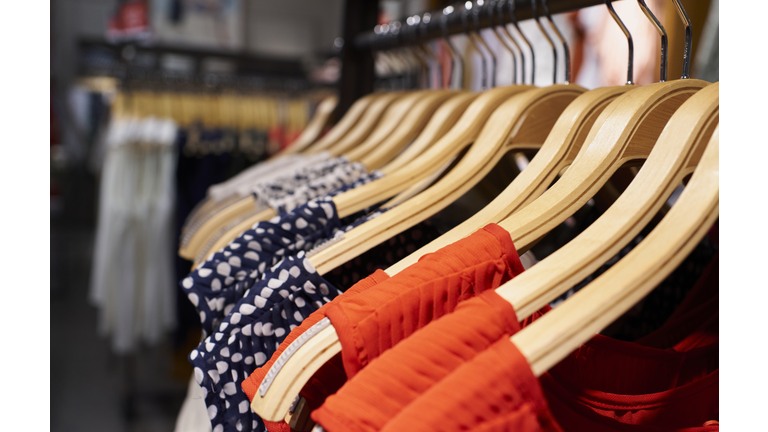 Close-up view of women's dresses hanging on clothes hooks in mall store rack, latest seasonal collection.