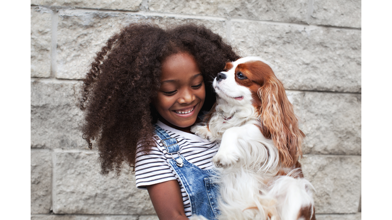 Portrait happy african american child holding pet dog on wall background
