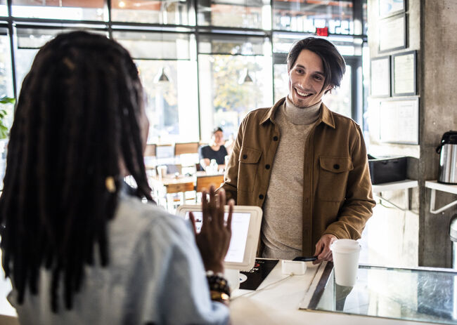 Young man using credit card reader at coffee shop counter