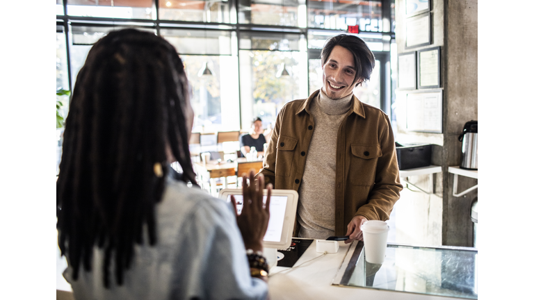 Young man using credit card reader at coffee shop counter