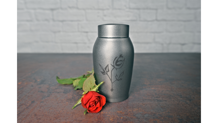 Funeral urn beside a red rose. Horizontal image with selective focus.