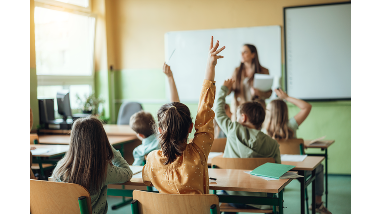 Students raising hands while teacher asking them questions in classroom