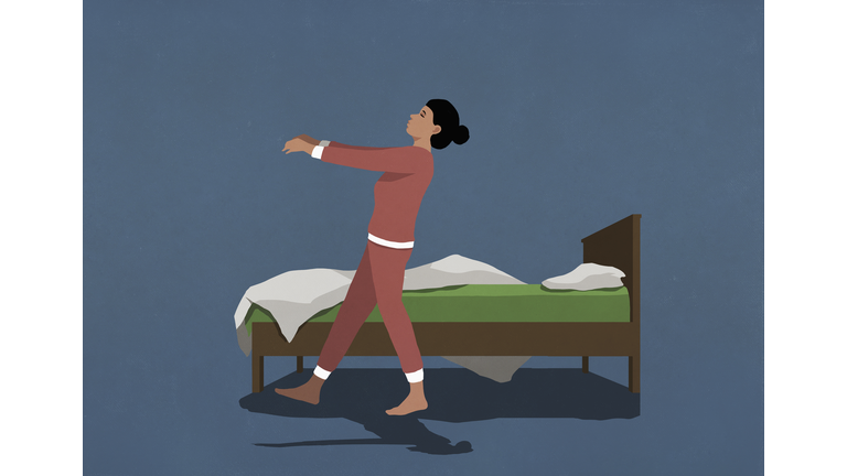 Woman in pajamas sleepwalking along bed in nighttime bedroom