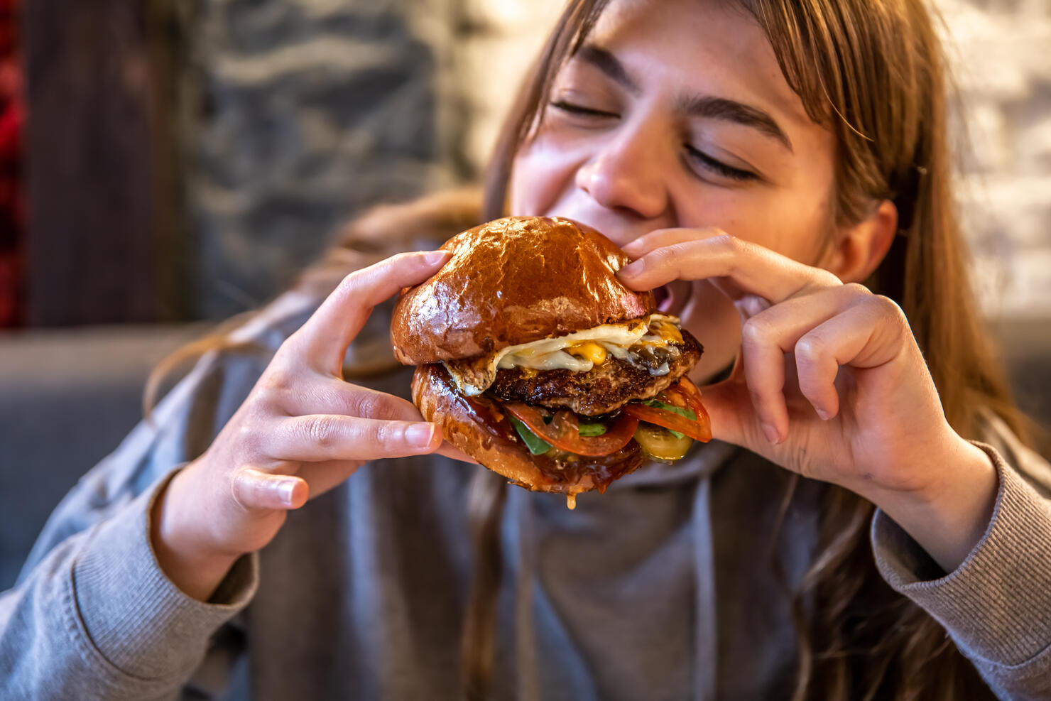 Big appetizing burger with meat in female hands in a cafe.