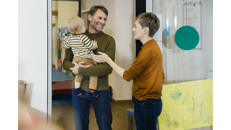 Pre-school teacher talking to father with toddler in kindergarten