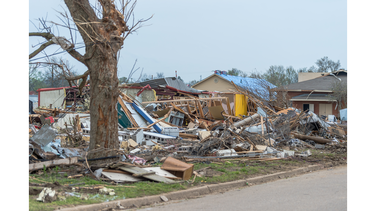 Destroyed homes with broken branches, personal belongings, and debris in the yard following a tornado