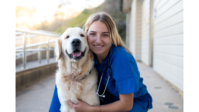 Veterinarian poses with golden retriever outside a clinic