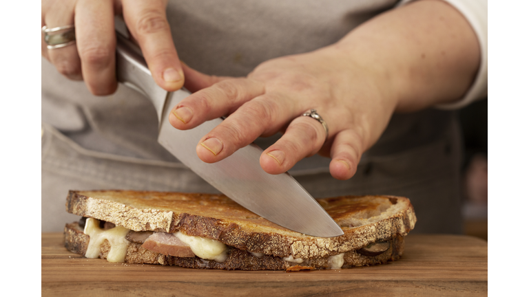 Close up of person slicing toasted sourdough cheese melt with chef's knife.