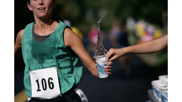 Woman running road race, grabbing cup of water, mid-section