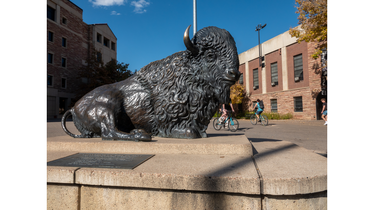 Students walking between classes in a plaza next to Folsom Field on the campus of the University of Colorado, Boulder. Bison statue in the foreground.