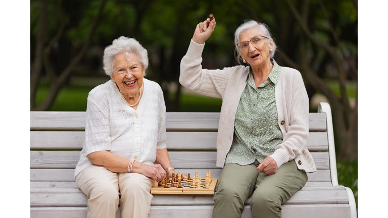 Elderly best friends playing chess in public park, having fun together.