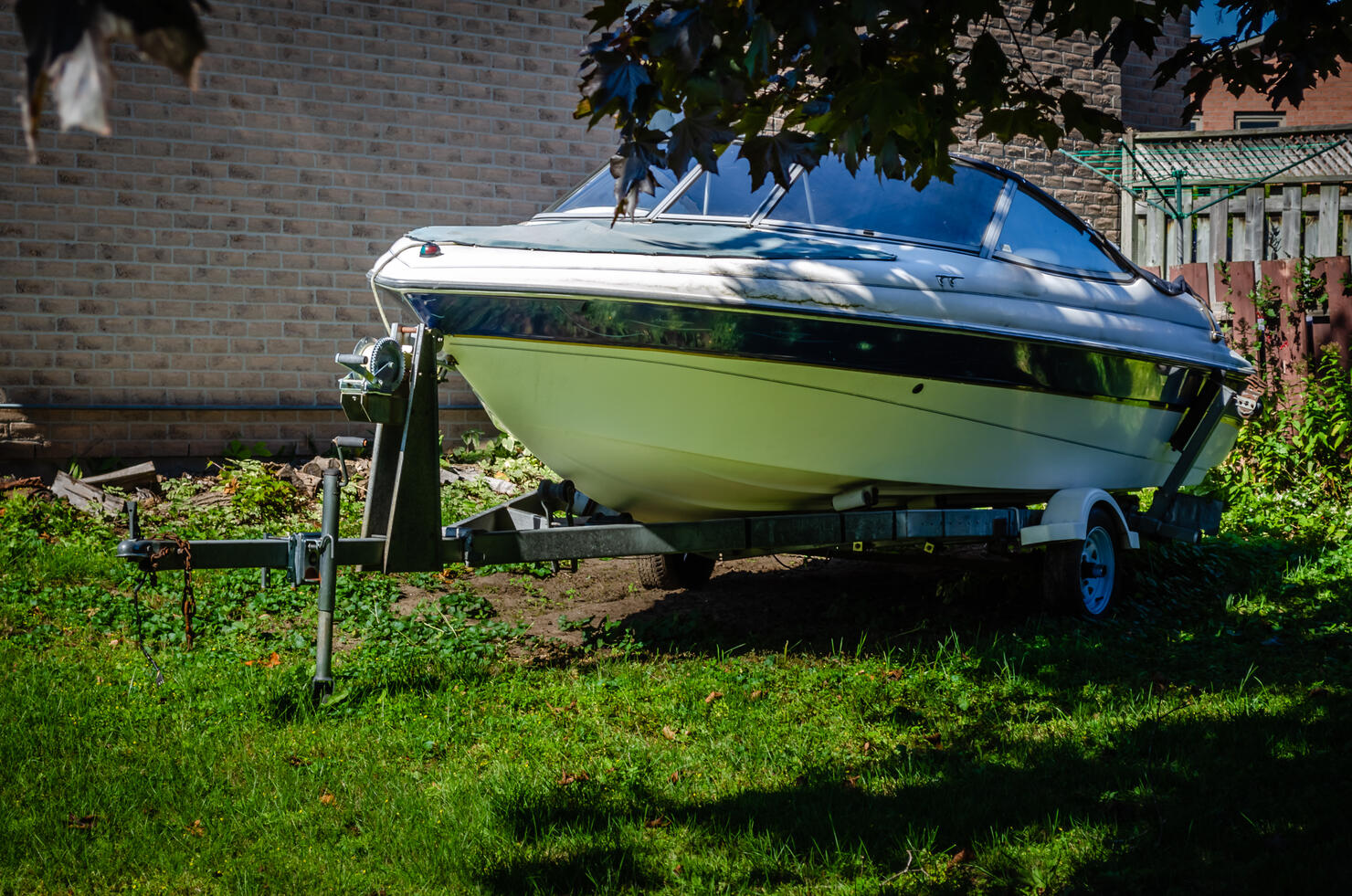 sport boat on a trailer parked in the shade in a yard next to a house,