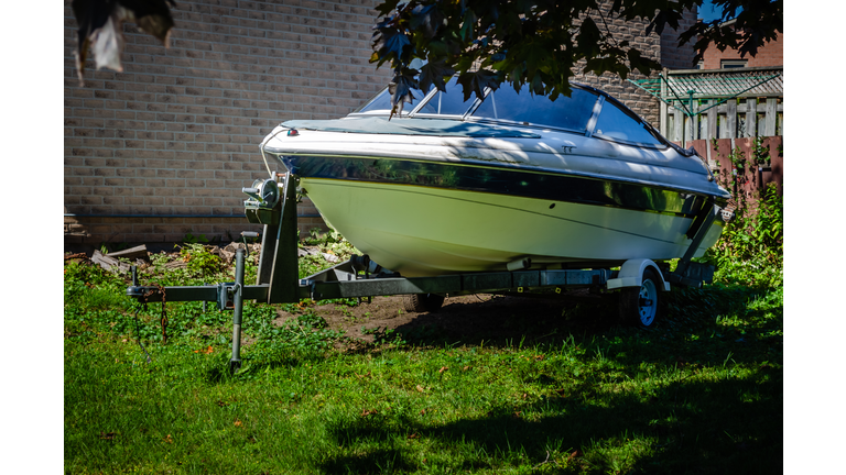 sport boat on a trailer parked in the shade in a yard next to a house,