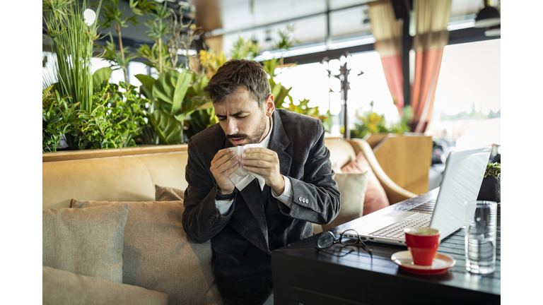 Sick Young Business Person has a Flu Virus and Sitting in Restaurant with his Laptop.