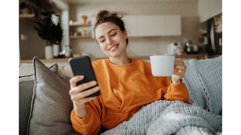 Young woman resting on sofa with cup of tea and smartphone.