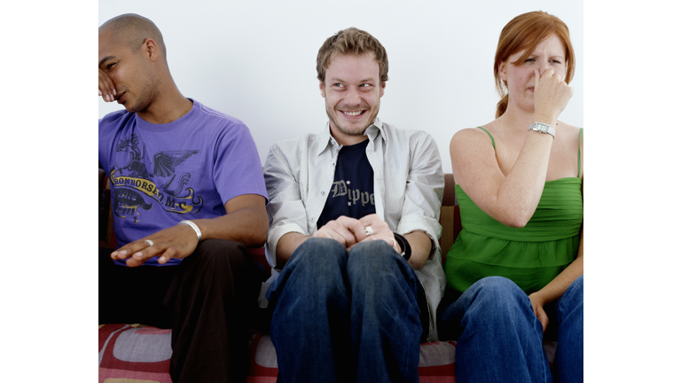 Young man, smiling, sitting between man and woman holding noses