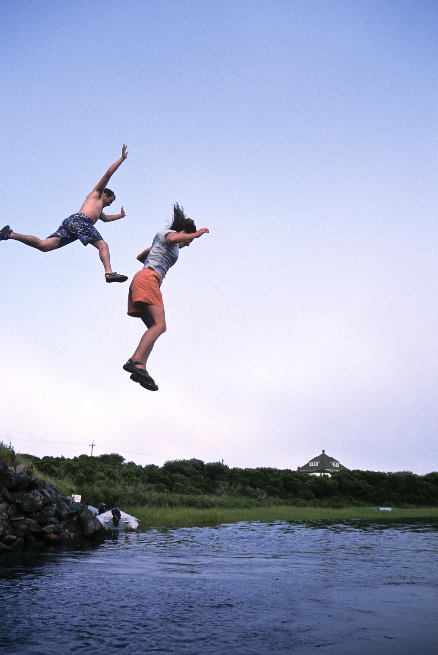 Two people jumping off bridge into water.