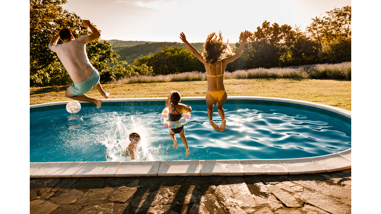 Back view of carefree family jumping in the pool at the backyard.