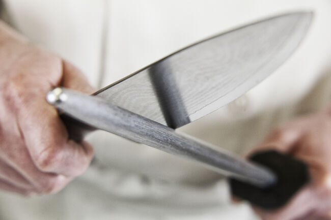 Close-up of a chef sharpening a large kitchen knife blade with a steel.