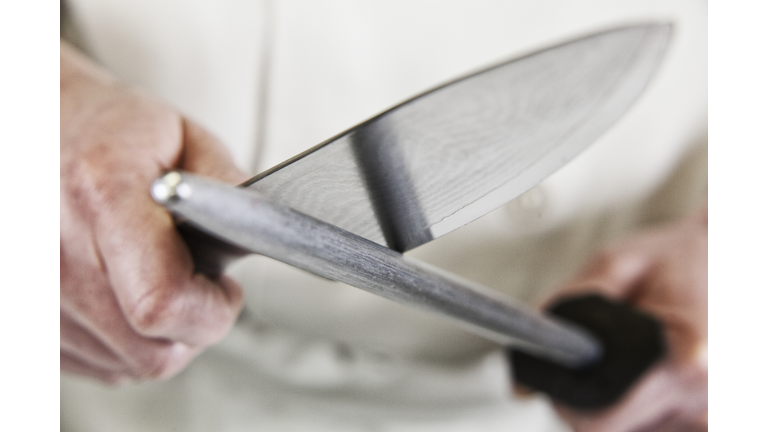 Close-up of a chef sharpening a large kitchen knife blade with a steel.