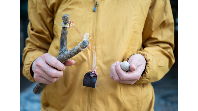 Cropped shot of woman holding a wood slingshot with clay bullet in her hands.  A slingshot works like a small catapult, with rubber strips holding a stone or other projectile sits.