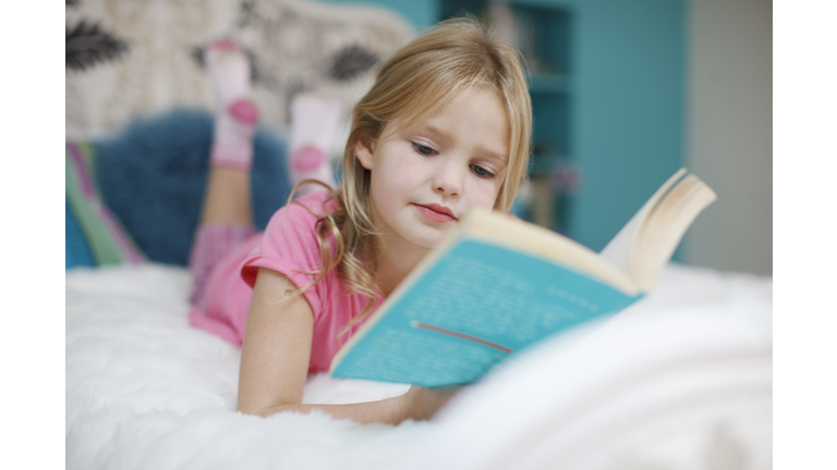 Girl laying on bed reading book