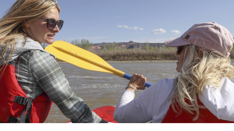 Two women kayaking down river pause to chat