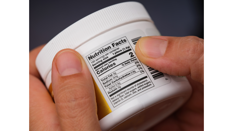 A woman holding jar with gums and reading a Nutrition Facts label at the back.
