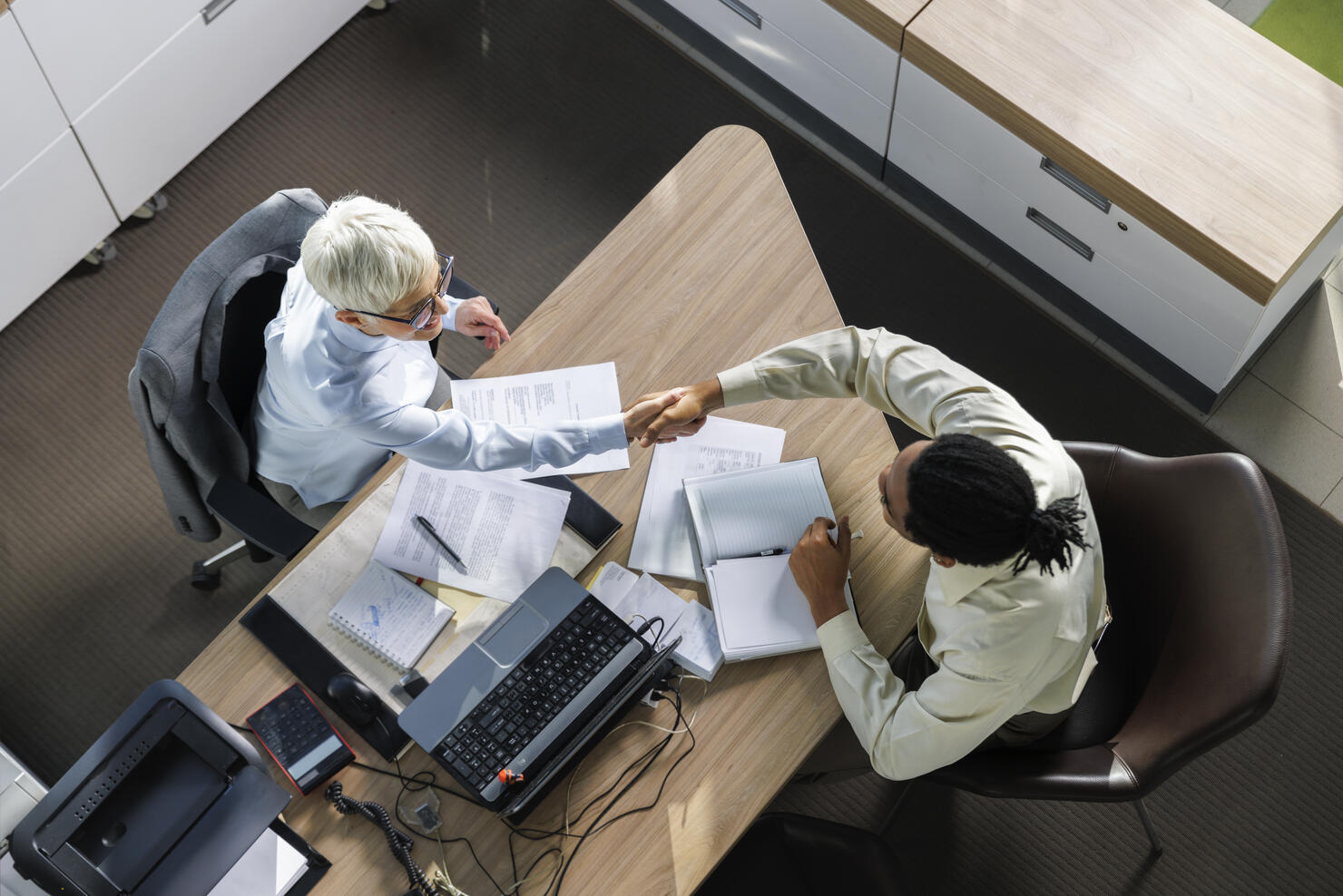 Interviewer shaking hands with candidate sitting at desk in office