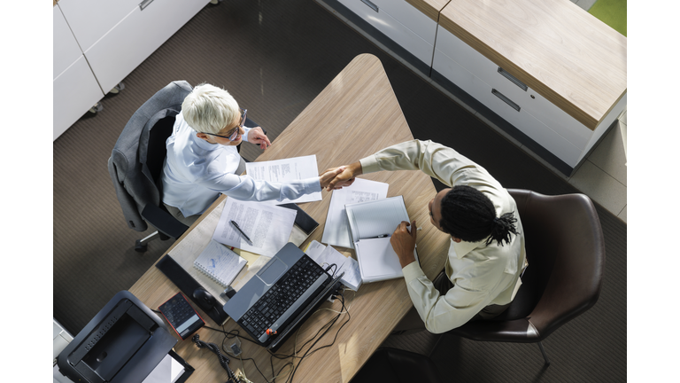 Interviewer shaking hands with candidate sitting at desk in office