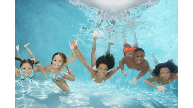 Children (6-13) swimming underwater in pool, smiling