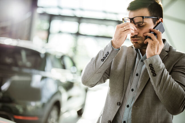 Businessman having a headache while talking on cell phone in a car showroom.