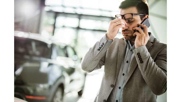 Businessman having a headache while talking on cell phone in a car showroom.