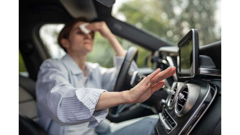 Woman drives car with broken air conditioner in hot weather wipes sweat on face.