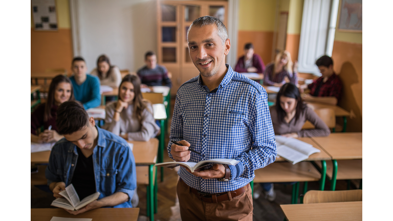 Happy high school teacher looking at camera during the class in the classroom.