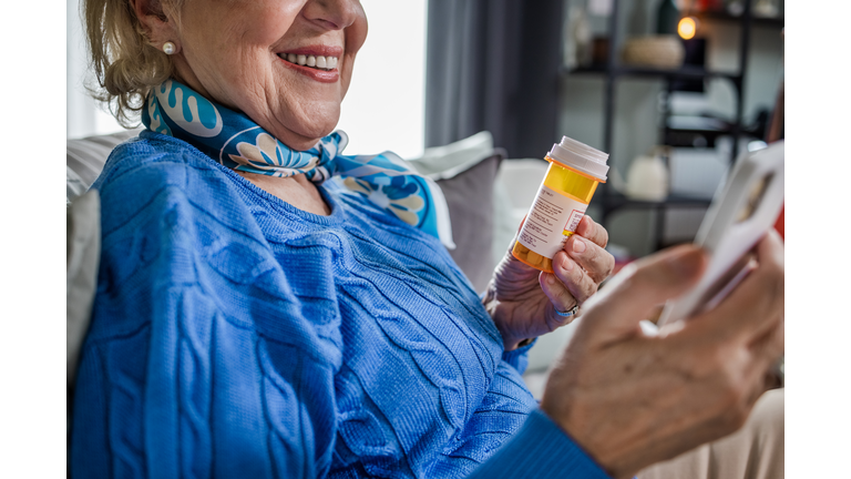 Close-up of a senior woman holding a pill bottle and a mobile phone
