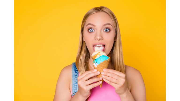 I like it! Head shot portrait of astonished shocked girl with wide open big eyes licking vanilla caramel ice cream with tongue having pleasure delight isolated on yellow background