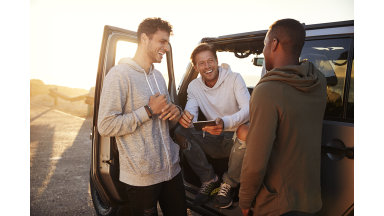 Three male friends on a road trip using a tablet computer