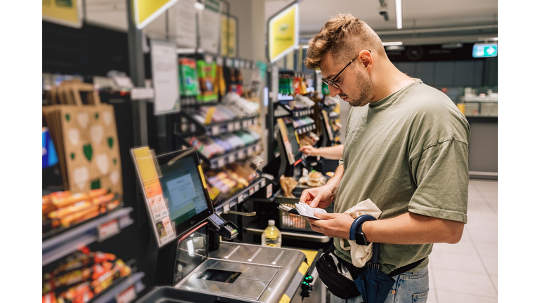 Man buying and paying money in the supermarket. Photo with people in the store during the shopping. Person is using contactless payment