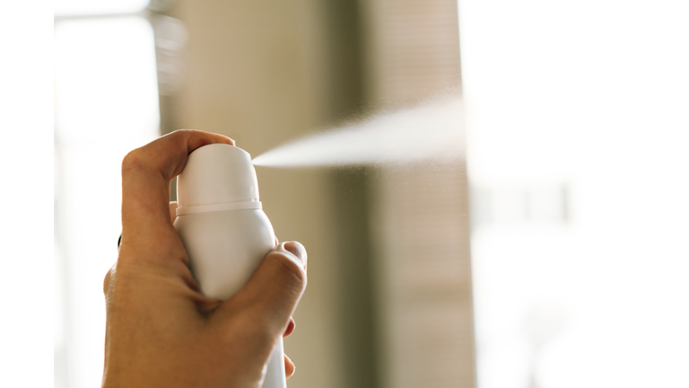 A bottle of white deodorant spray spraying a jet of air in a woman's hand