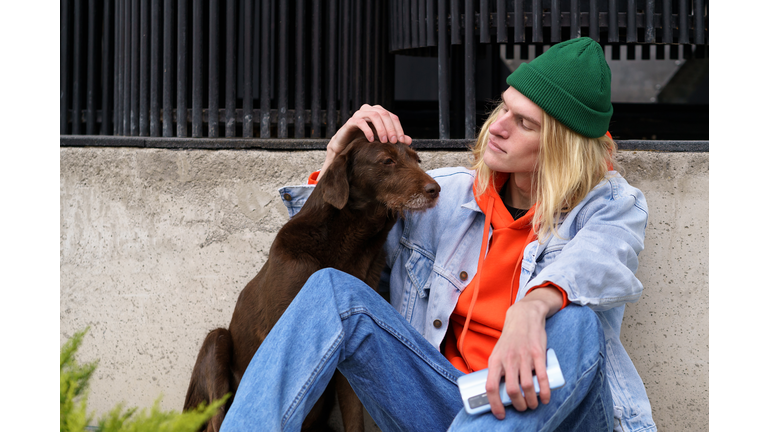 Hipster guy sitting on street with upset stray dog, problem of homeless animals