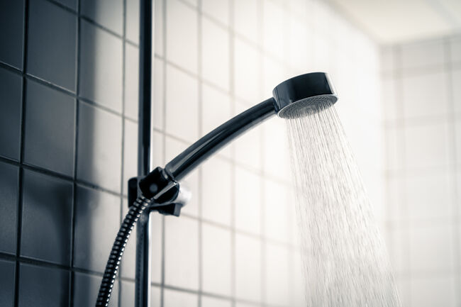 Shower head. Dark dramatic scary light. Cold water running in bathroom. Public washroom in hostel, gym or bad hotel. Hot flow. Black faucet. Emotional, horror or dirty.
