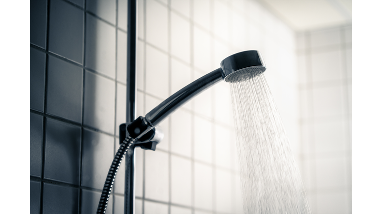 Shower head. Dark dramatic scary light. Cold water running in bathroom. Public washroom in hostel, gym or bad hotel. Hot flow. Black faucet. Emotional, horror or dirty.