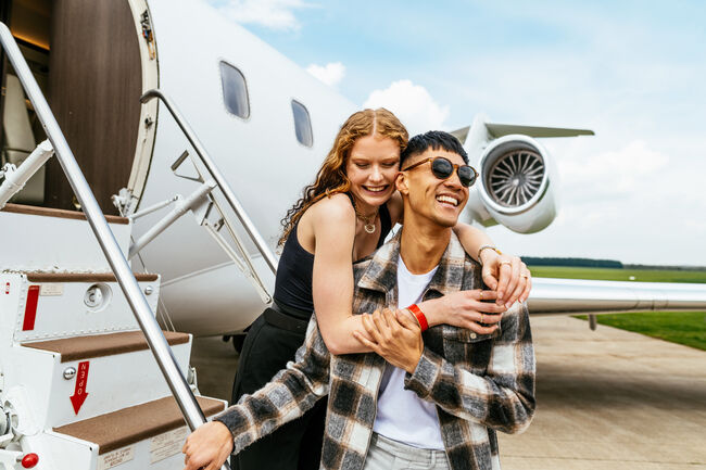Young multiethnic couple enjoying travel by private jet. Young successful people in front of the private jet.
