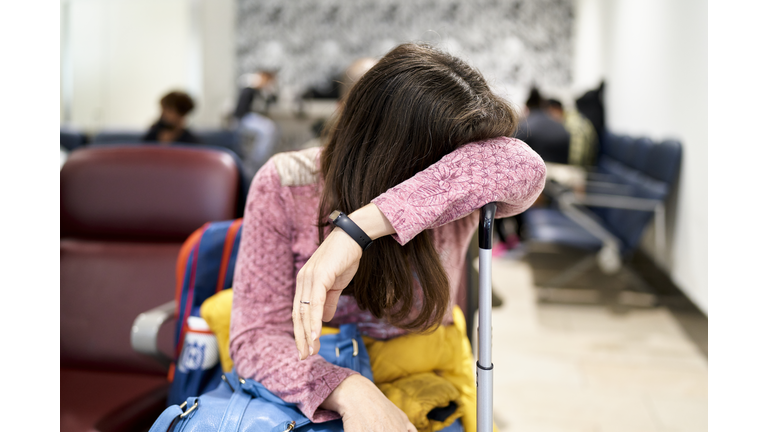 A married white woman waits in a tired position with her suitcase in the airport lounge