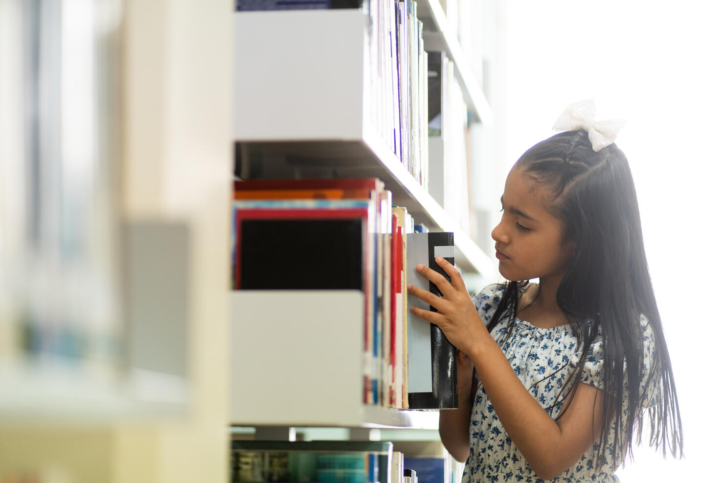Little girl taking book from bookshelf