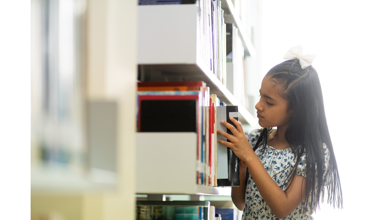 Little girl taking book from bookshelf